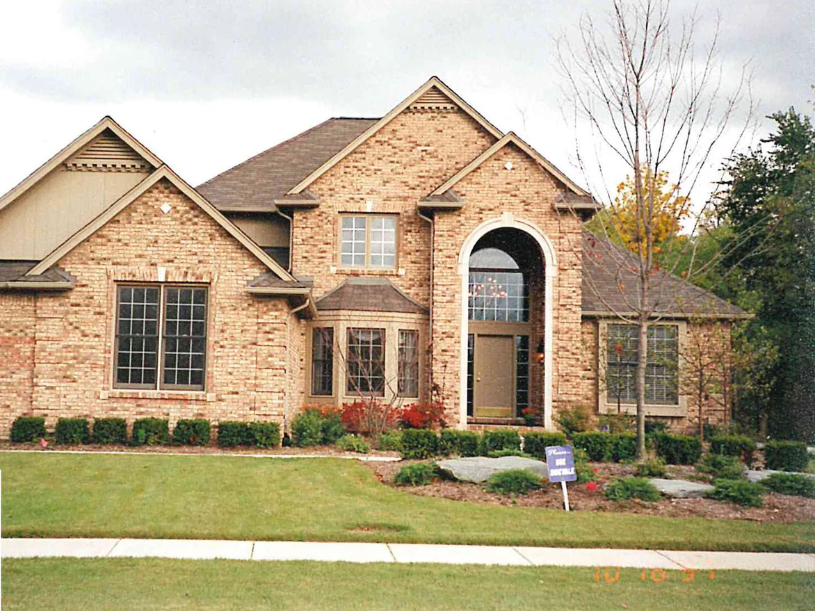 The front of the two-story house in 1997, its brick a warm tan across the steep gables, the bay window and the tall arched entry