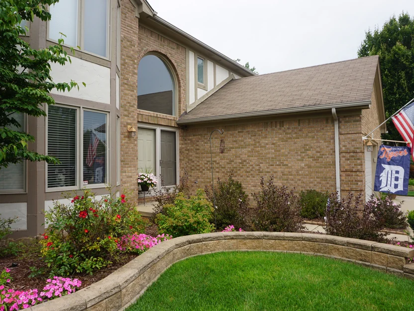 The entry and the garage wall in 2019 seen across the planting bed, the brick carrying one blend around the corner
