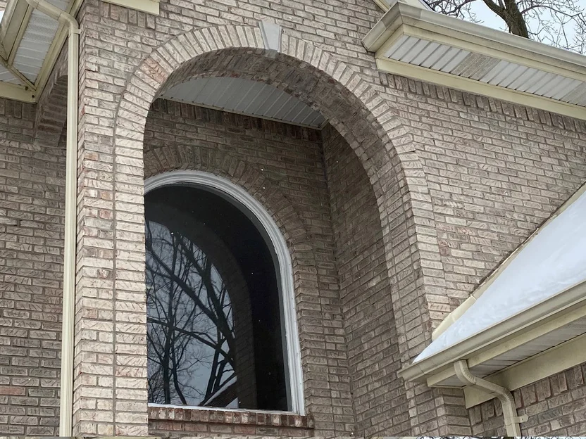 The entry arch in 2021 with the arched window fitted and white trim run around it, the brick above the opening even from the arch ring out to the corner