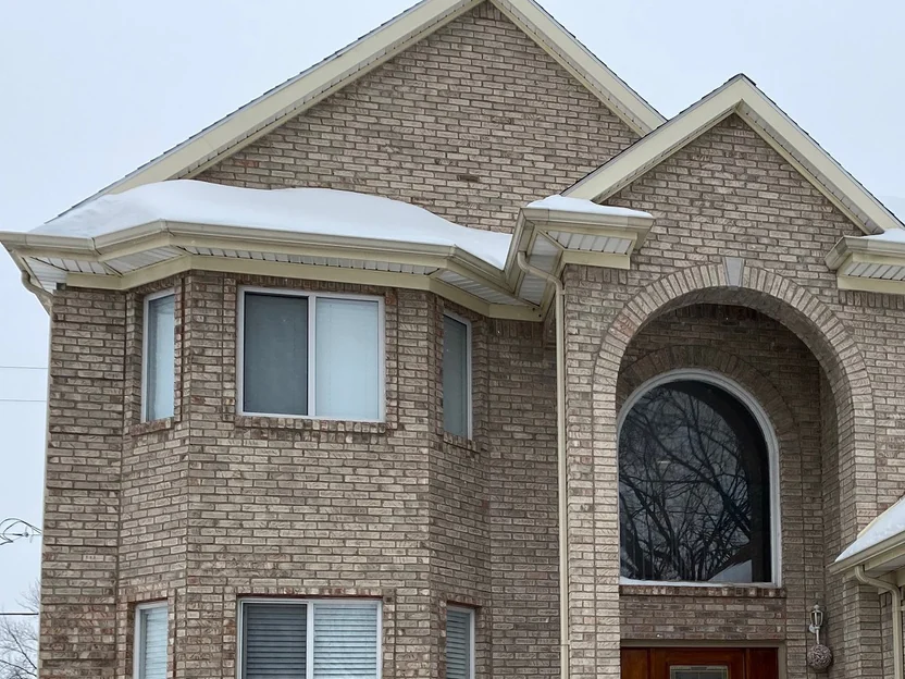 The same front bay and gable in 2021, finished with cream soffit and fascia and snow on the roof, the brick carrying one range across both gables