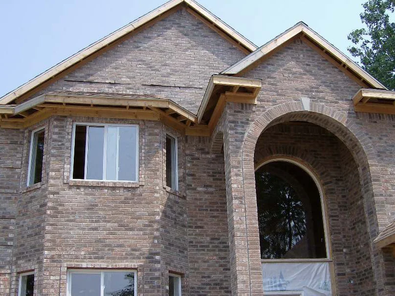 The front bay and gable of the house in 2007, still under construction with open window openings and bare eave framing, the brick running pink, tan and dark grey from course to course