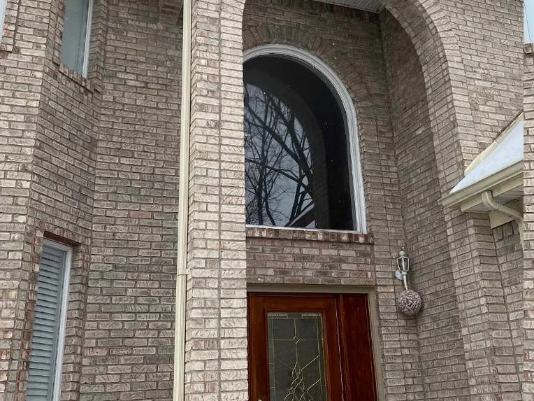 The same arched entry bay in 2021 with a stained wood front door and a wreath, the arch ring and the wall beside it reading as one blend