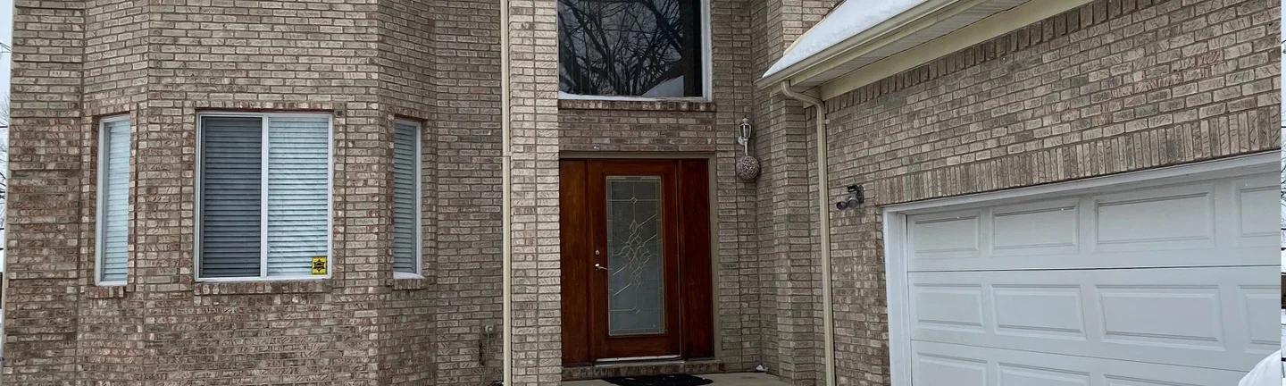 The front of the Sterling Heights house in 2021, tan brick running in one range across the bay, the arched entry and the garage