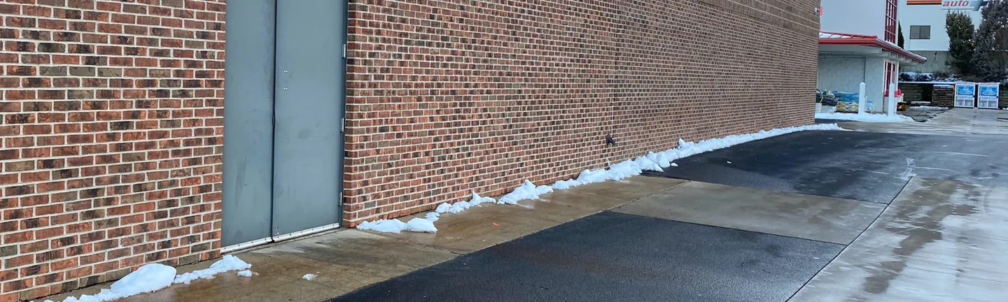 The side wall of the store addition in 2020, red brown brick running past a grey steel double door under a cream fascia