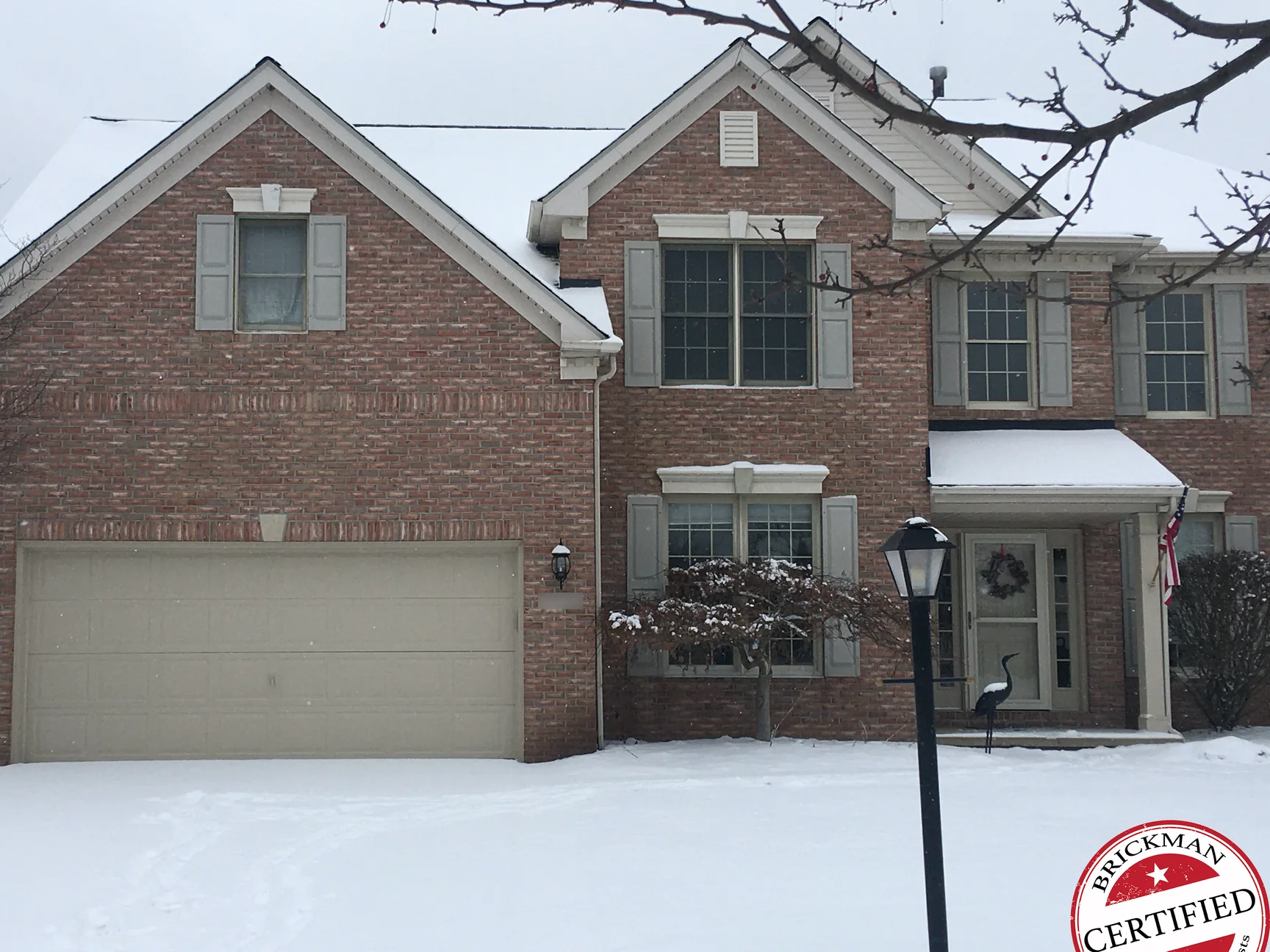 The whole front of the house in 2020 under snow, the gable, the center bay and the garage wall reading as one pink salmon brick, with the certification stamp in the corner