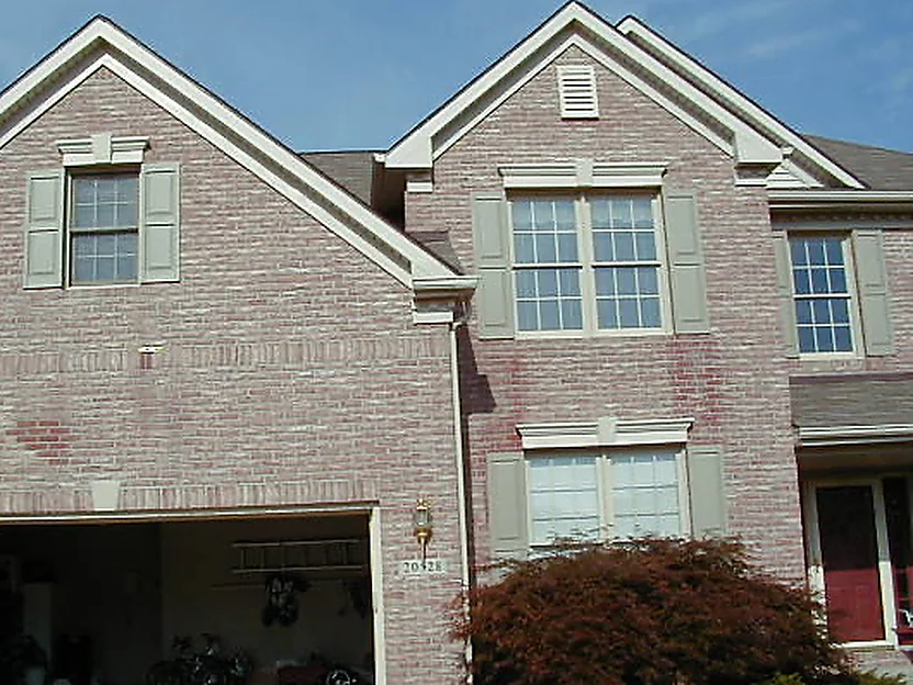 The front of the two-story house in 2005, pink brick with darker mottled units around the gable and the window bays, tan shutters at every window