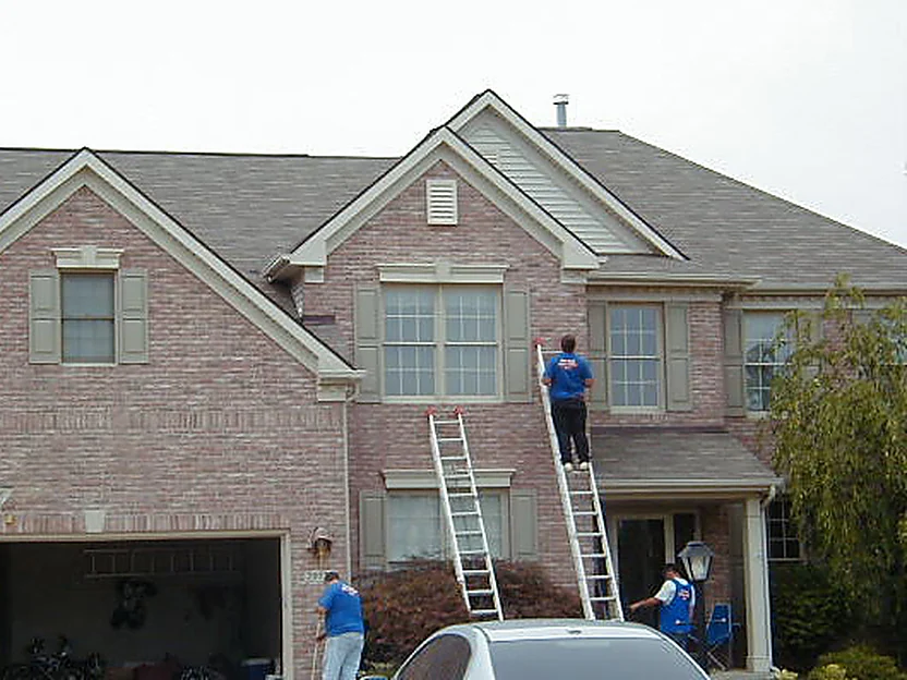 Two applicators on extension ladders working the brick beside the center window bay in 2005, a third at the garage wall below