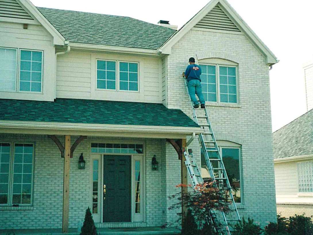 An applicator on an extension ladder at the right-hand gable of the house in 1998, working on the brick beside the arched upstairs window