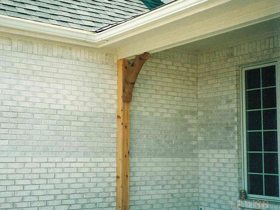 The porch corner in July 1998, a band of darker brick running through the light wall to the right of a cedar post and bracket, with the camera date burned into the corner