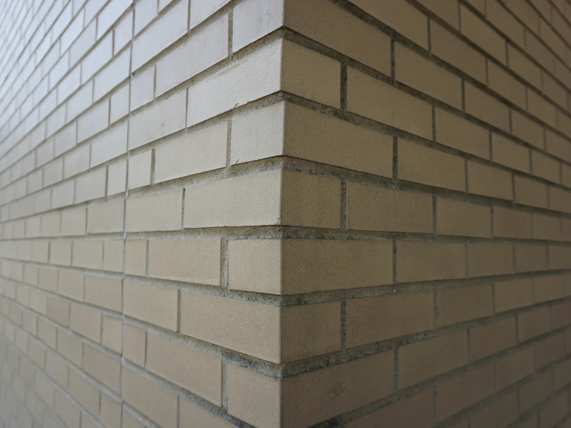 Close view of an outside brick corner in 2019, the units an even buff and tan with recessed grey mortar joints