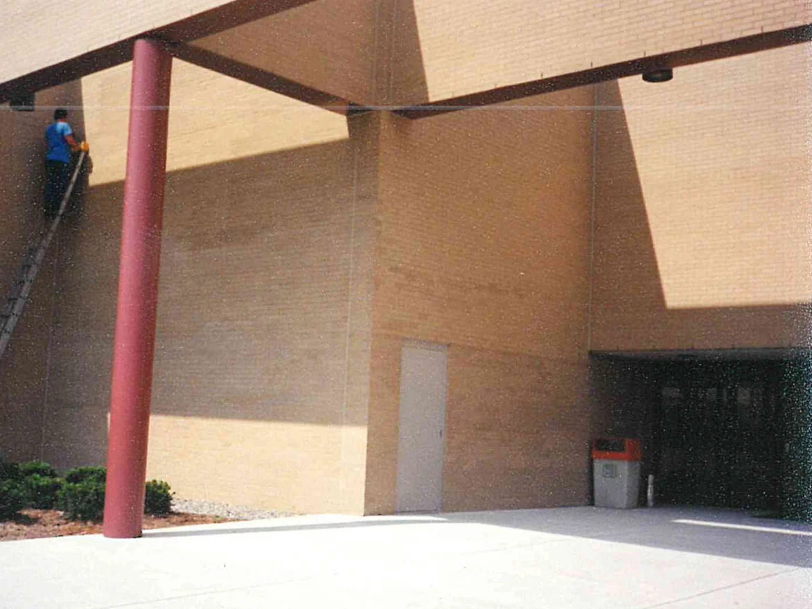 An applicator on a ladder working the brick under the entrance canopy in 1999, a maroon steel column and beam framing the recessed wall