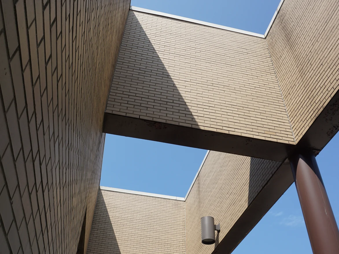 Looking up through the canopy openings in 2019, brick soffits and wall panels framing rectangles of sky beside a maroon column
