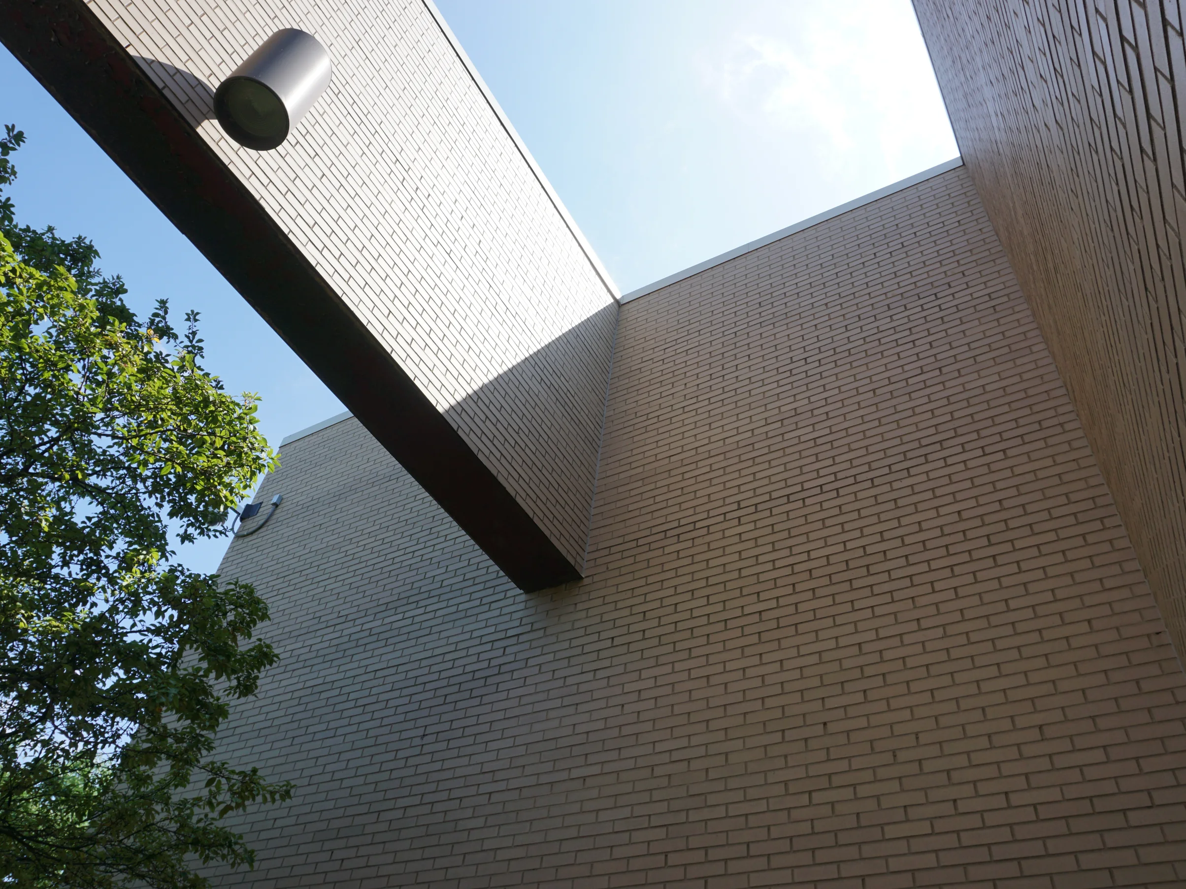 Two brick wall planes meeting at an inside corner in 2019, under a projecting canopy beam and a cylindrical light fitting
