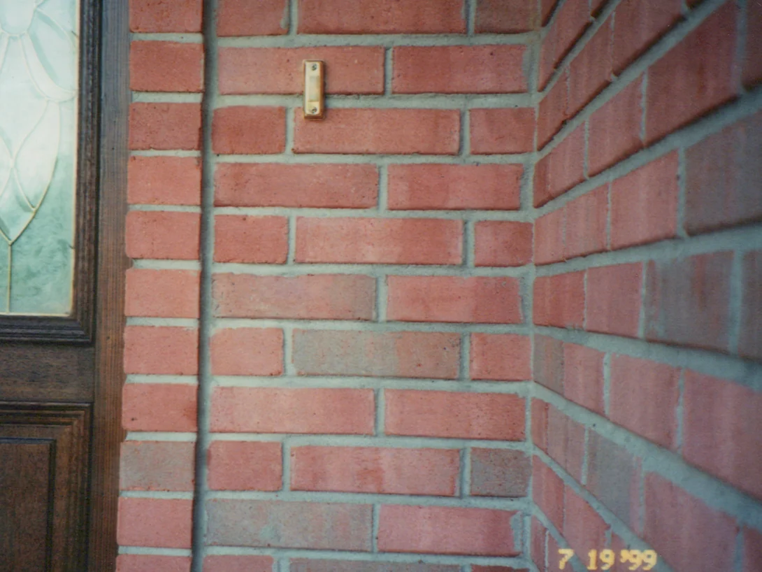The brick beside the front door in July 1999, a brass doorbell on the wall and several units reading grey and pink against the red around them