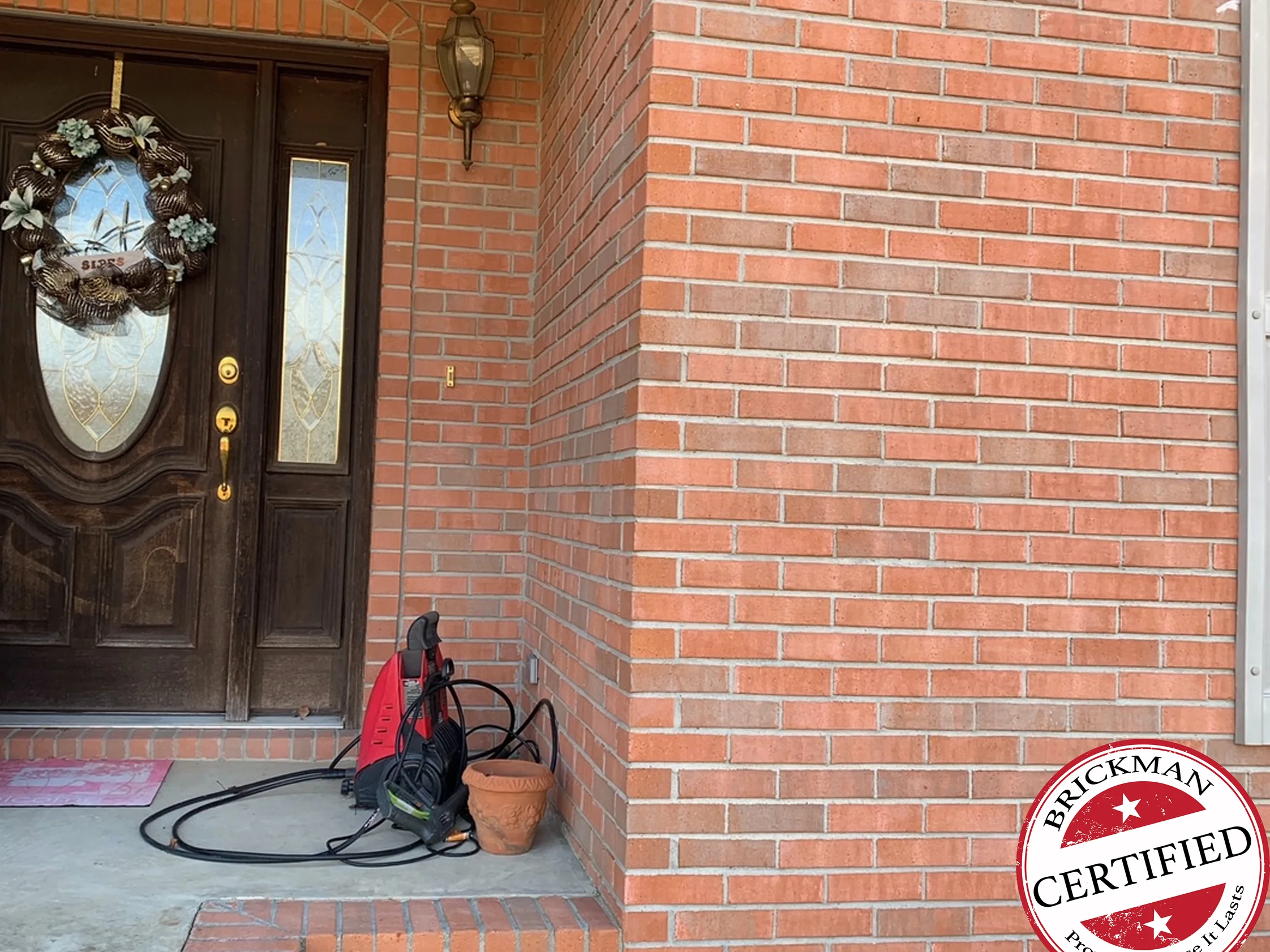The front entrance in 2020, a dark wood door with a wreath and leaded sidelights, the brick beside it and around the corner in one red range, with the certification stamp in the corner
