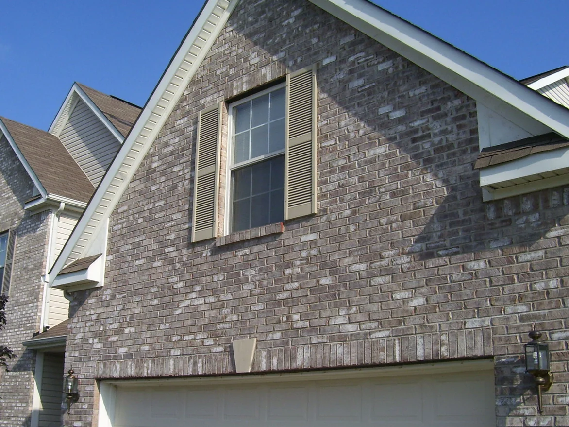 The same garage gable on the same day in August 2009 after staining, the brick now a grey and cream blend against a clear sky, the front gable of the main house beside it in the same range