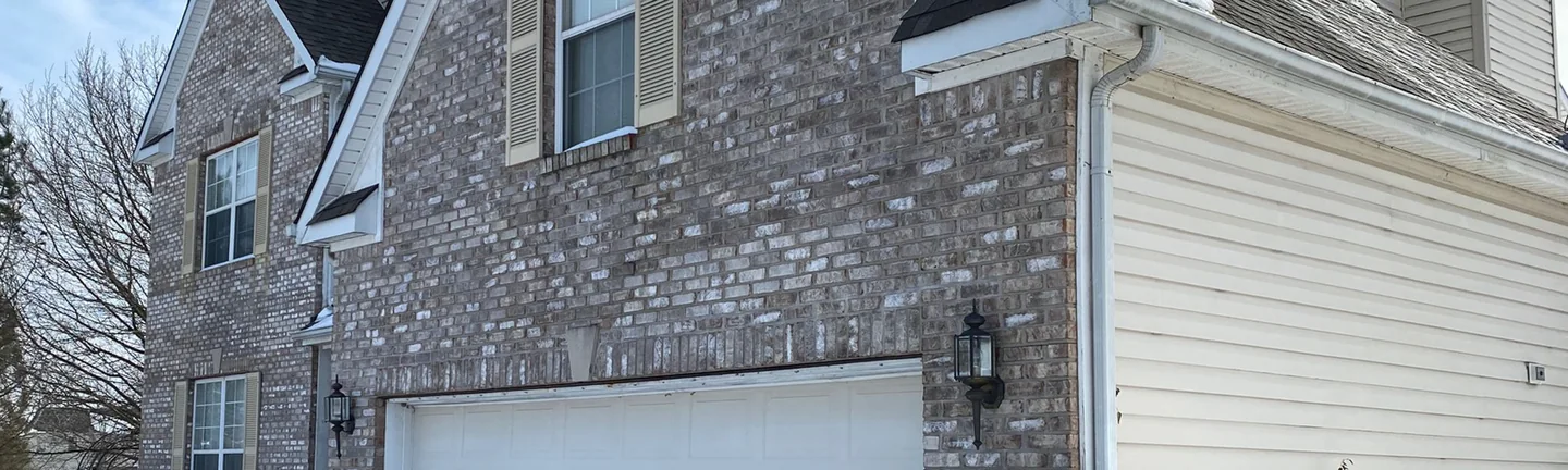 The garage wing of the house in 2021, grey and cream brick around a shuttered window with snow on the roof above it