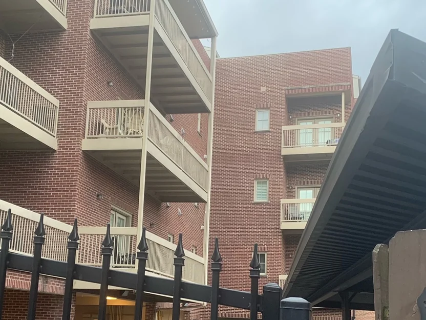 The balcony courtyard in 2021, red brick even across four levels of decks behind an iron fence and a dark metal carport