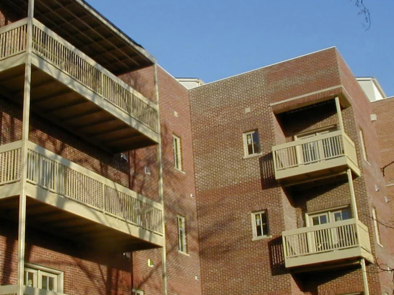 The balcony courtyard in 2004, a man on an extension ladder at the foot of a brick pier below four levels of railings
