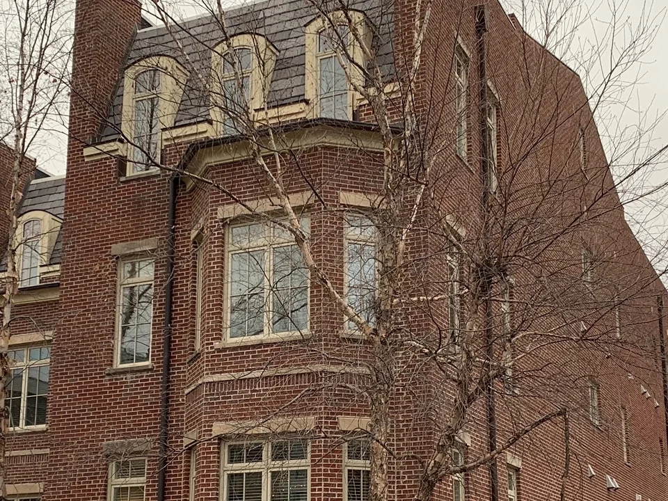 The corner bay of The Row in 2021, red brick carrying from a rusticated stone base past two levels of windows to dormers set in a slate roof, bare trees in front
