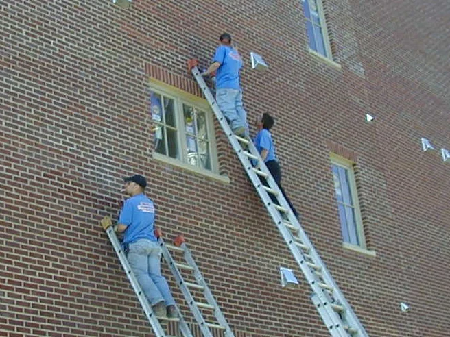 Three applicators on extension ladders in 2004, working stain into the brick by hand beside the upper windows