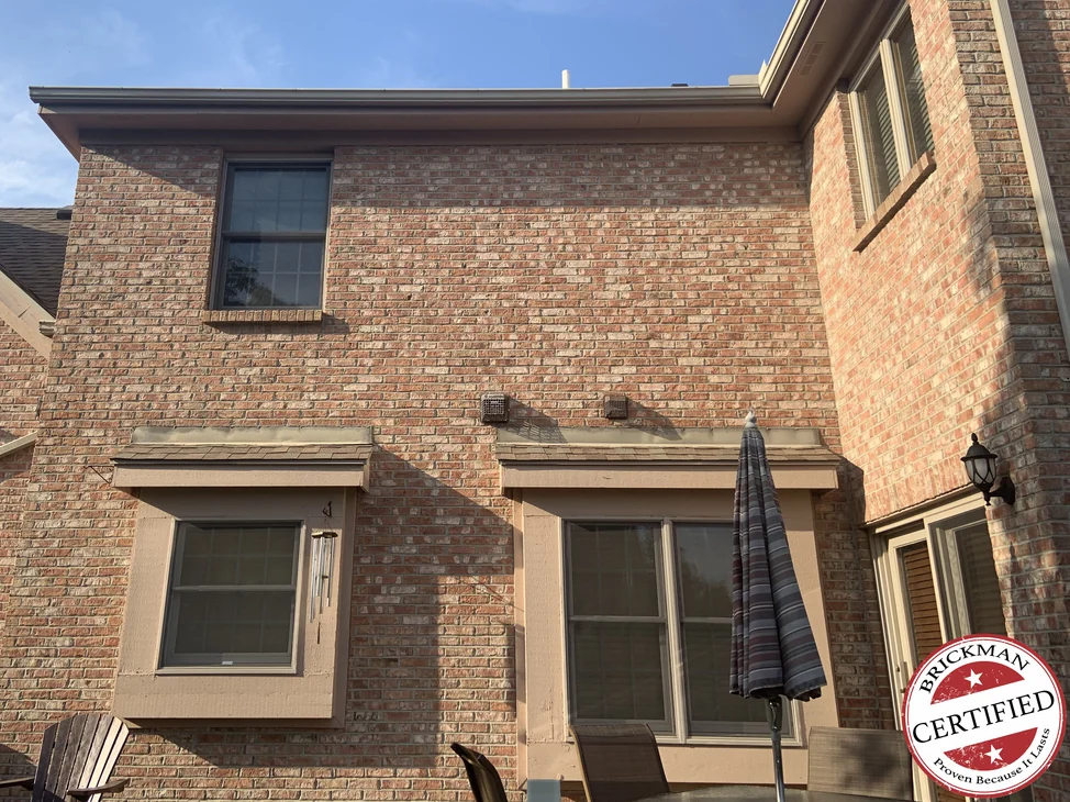 The back of the house in 2019, the rear wall and the corner beyond it reading as one range of tan, cream and red brick, with the certification stamp at the corner of the frame.