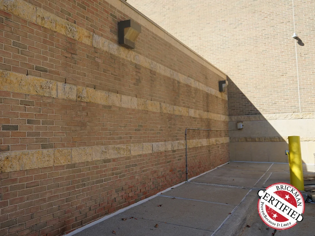 A banded wall in 2019 running away from the camera, red brick between wide lighter courses with rain staining down the face, the frame carrying the Brickman Certified stamp