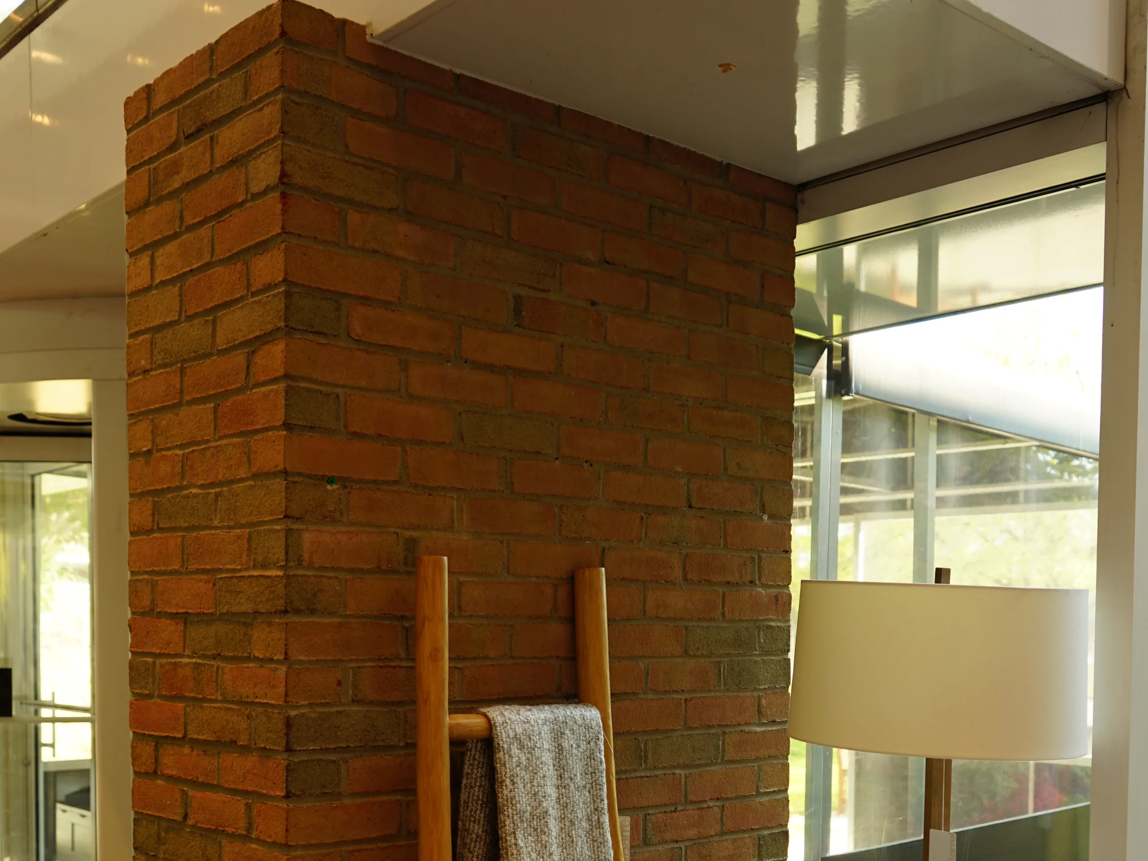 A red brick pier standing inside the glazed entrance vestibule in 2019, a blanket ladder and a floor lamp set against it
