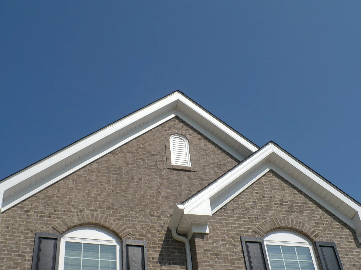 The same two gables in 2012 after staining, the peak brick darkened into the range of the wall under it, against a clear sky