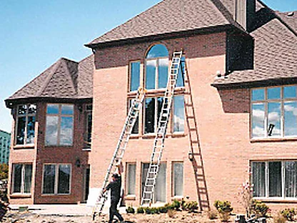 Two extension ladders against the rear wall in 1997 with an applicator at the foot of one, the brick around the tall arched window part way through being stained