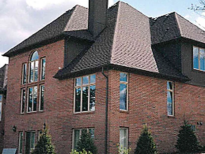 The rear of the house in 1997 before staining, red brick under a hipped roof and chimney, with darker units clustered unevenly through the wall between the tall arched window and the ground floor