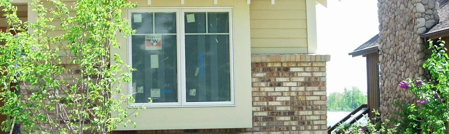A bay window and a pale buff brick pier on the house in 2008, before the stain, with water beyond the far corner