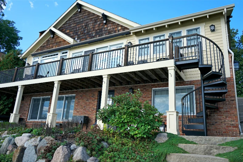 The walkout side of the house in 2019, the brick lower level a warm red and brown under a raised deck and a spiral stair
