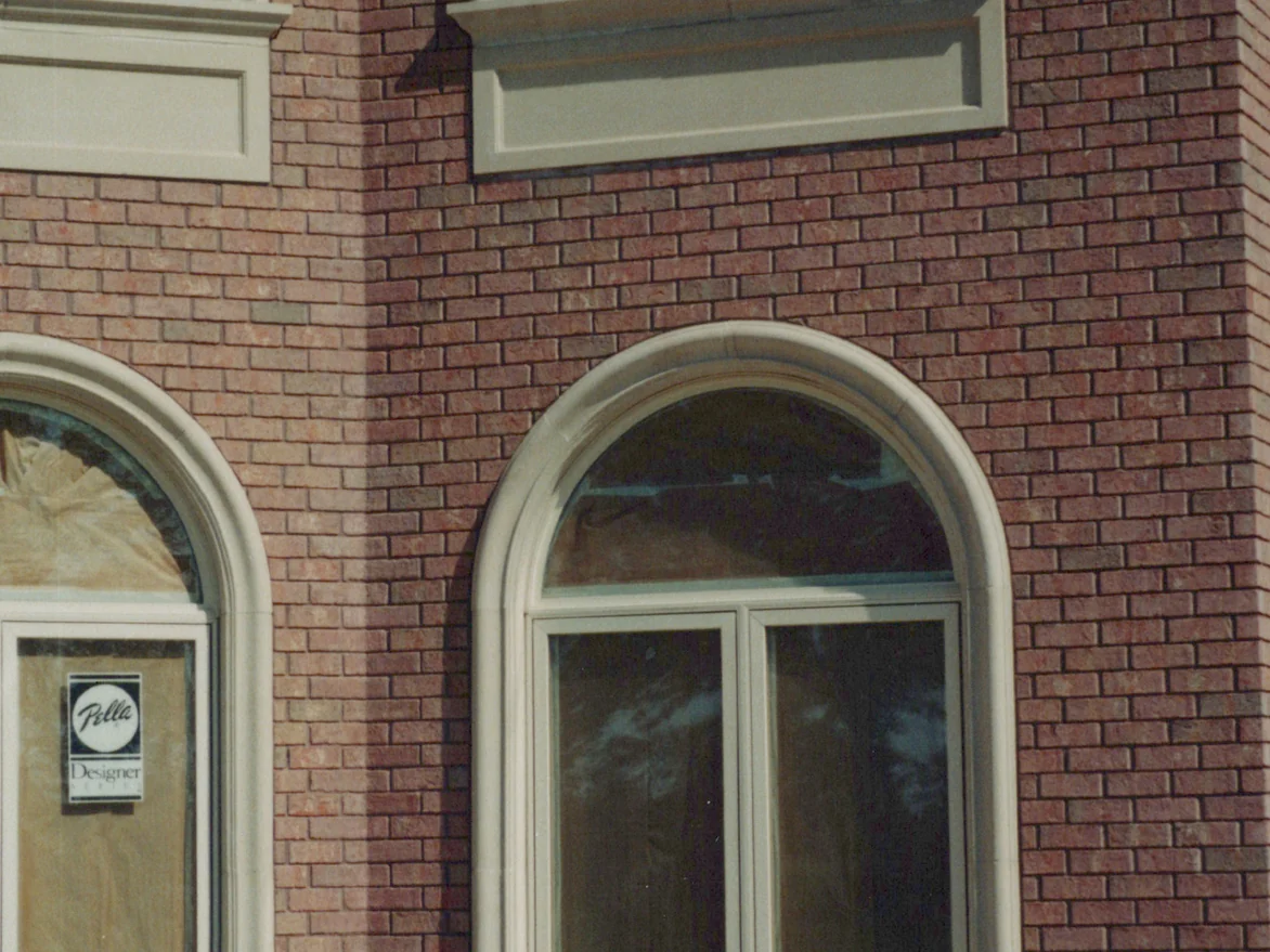 The outside corner pier in 1999 between two arched windows in cast stone surrounds, the brick at the corner reading in the same red as the wall, with new window labels still on the glass