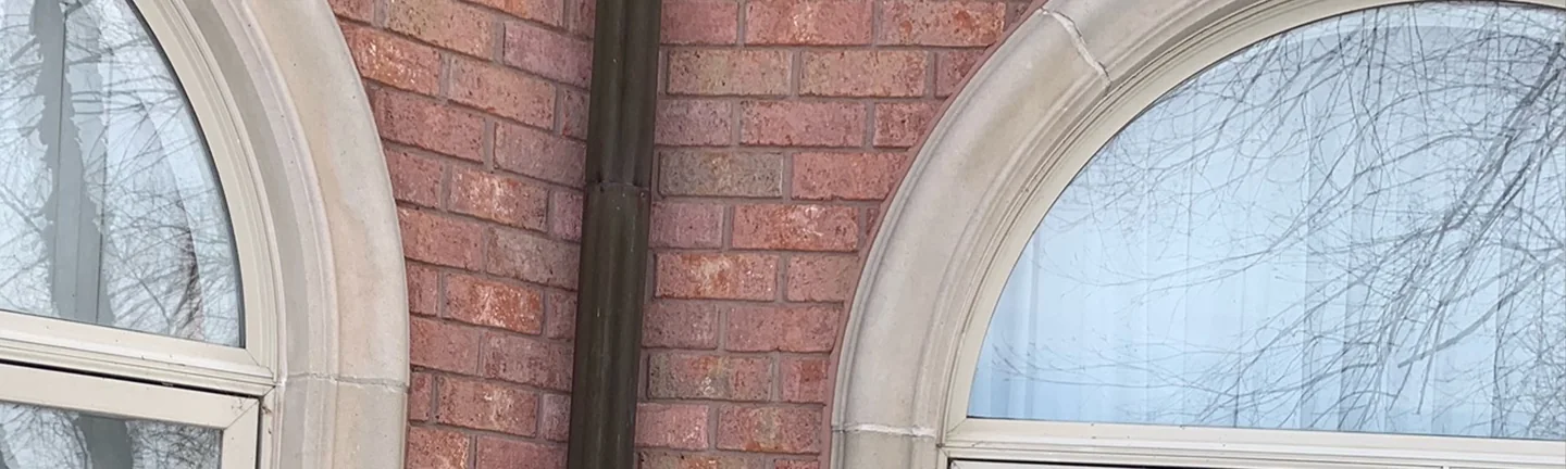 The inside corner of the Warren building in 2021, red brick either side of a dark downspout between two cast stone arches