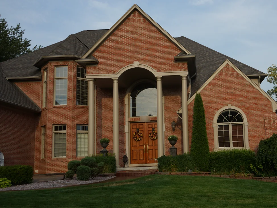 The front of the house in 2019, red brick reading as one range across the entrance gable, the columned portico and the bay window