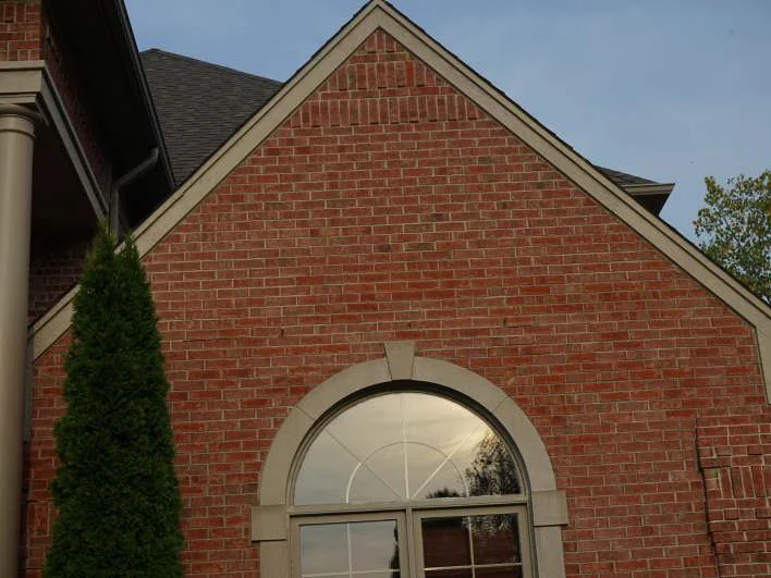 The same side gable over its arched window in 2019, the brick one even red range from the peak down, with an evergreen grown up beside it