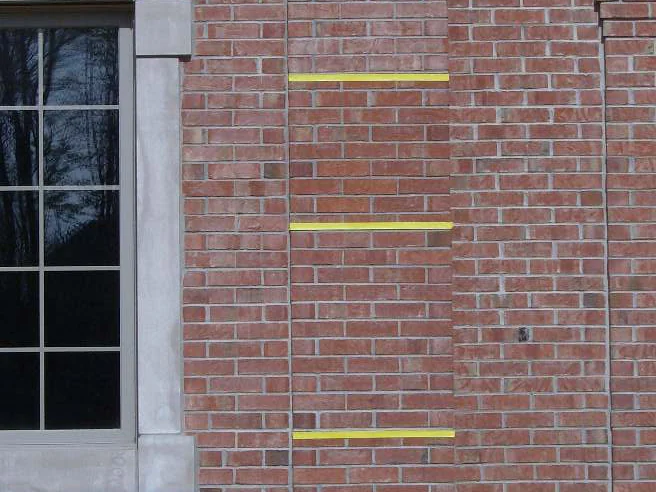 The reverse test panel in 2007, three strips of yellow tape marking a patch of brick beside a window, the wall around the patch already stained a deeper red