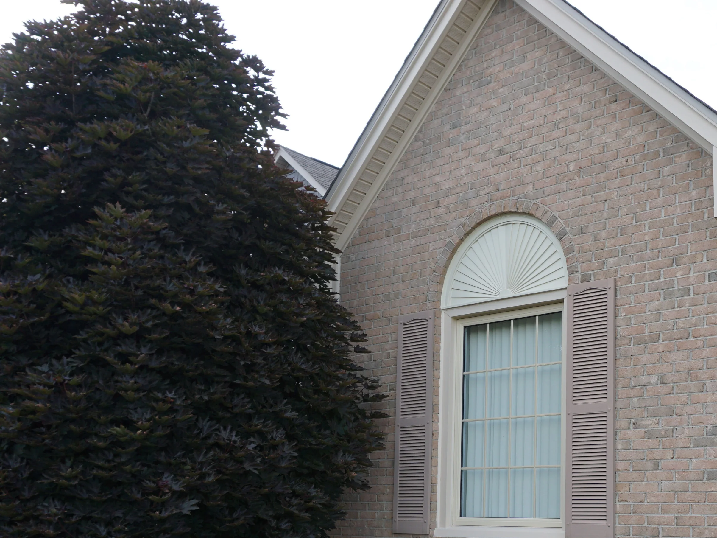 The brick gable at the end of the house in 2019, an even light tan and grey range running up to the eaves around an arched window