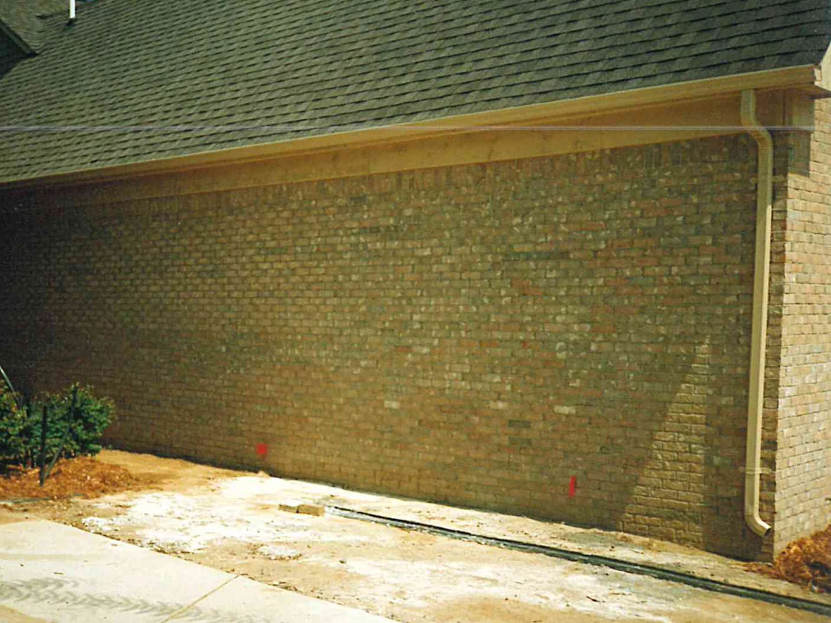 A long brick wall beside the driveway of a newly built house in 1996, dark units running through the tan range under the roof overhang