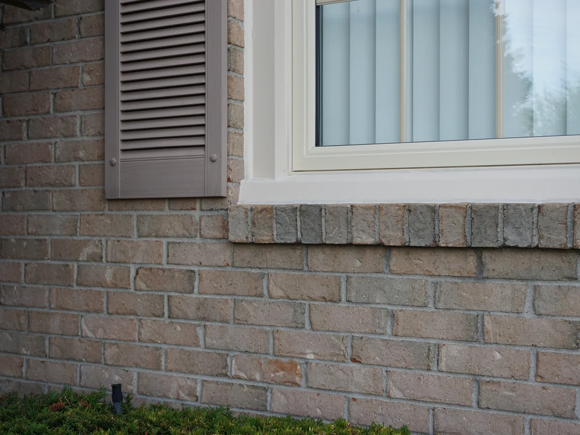 A rowlock window sill and a louvred shutter set in the brick in 2019, the units under the sill the same tan and grey range as the wall
