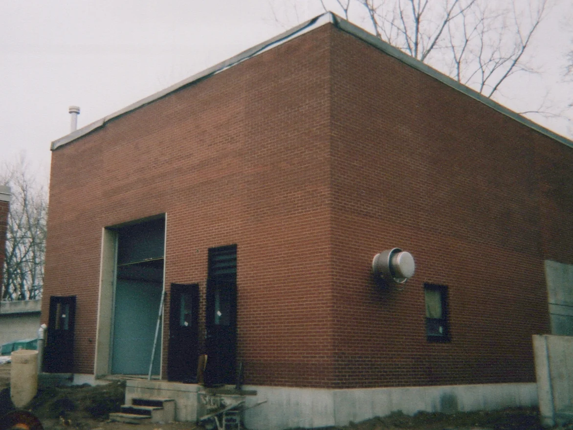 The corner of the new brick building in 2003 before staining, bands of lighter and darker red brick running across both walls above a bare concrete foundation