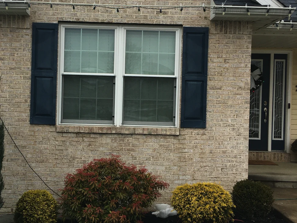 The gable end of the Waterford house in 2020, one range of light brick around a double window with navy shutters and a string of lights along the eave.