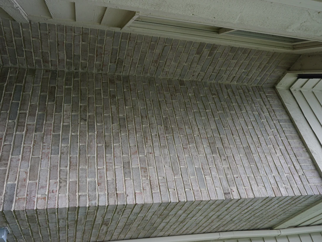 Looking steeply up an inside corner of the wall under a white soffit, the brick a pale gray and pink range with wide cream joints