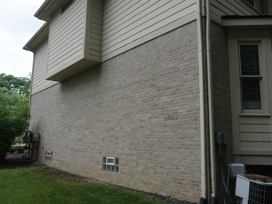 The side wall of the house in 2019 running the length of the frame, buff brick with scattered darker gray units under lap siding