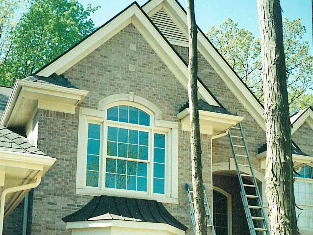 Two ladders leaning on the front gable in 1999, the brick around the arched window blotchy in gray and tan