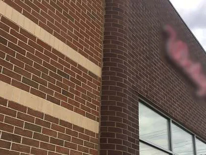The wall from a sharp angle in 2019, courses of red brown brick and a buff band running along to the rounded corner and the return wall beyond it