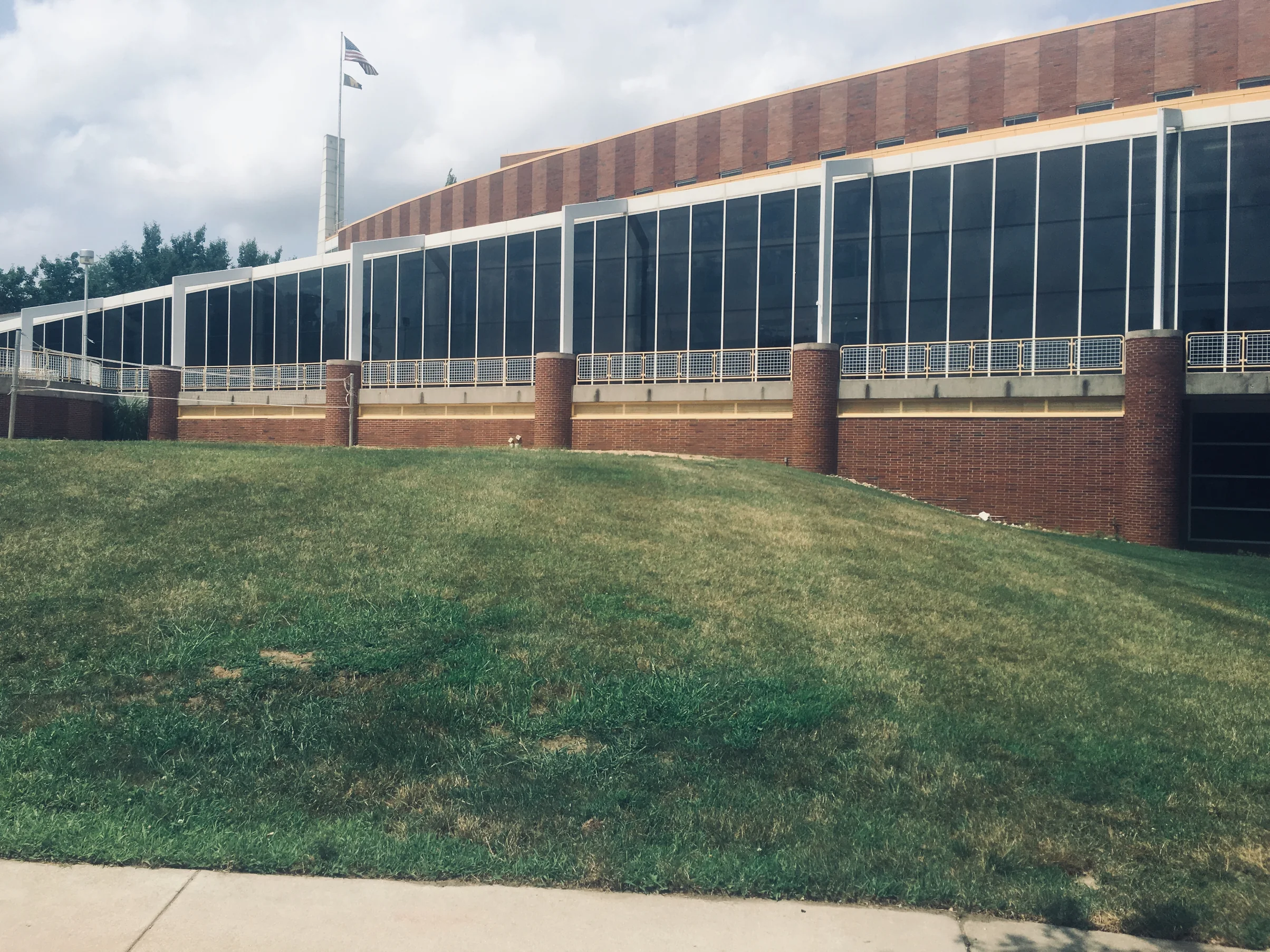 The long elevation in 2019, a continuous glazed wall over a red brick base and round brick columns, with a curving band of brick above it at roof level