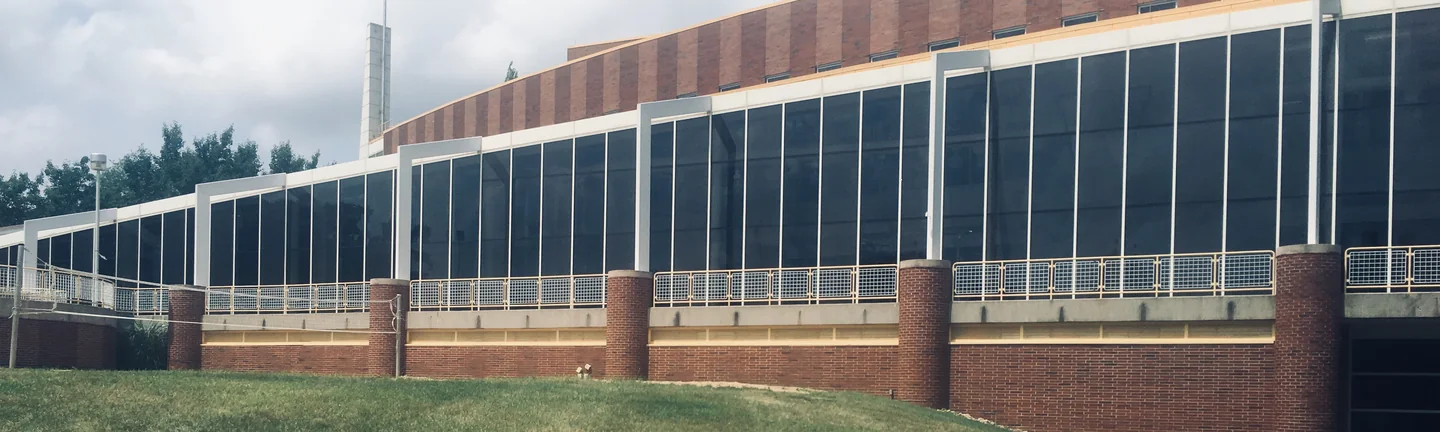 The campus building in 2019, a long glazed elevation running above a red brick base with round brick columns