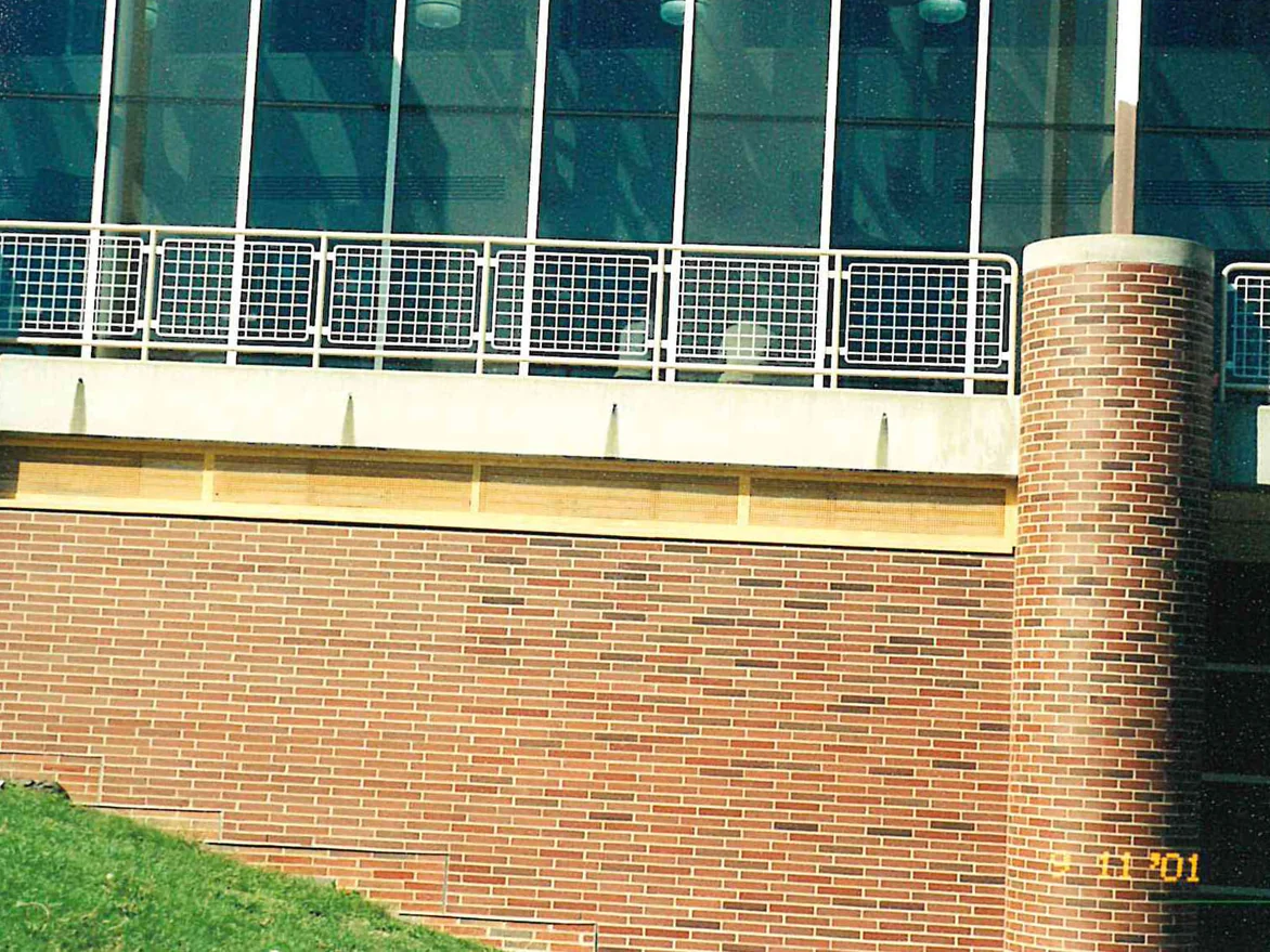 The brick wall under the terrace rail with a round brick column at the right, the glazed wall above it and lawn at its base